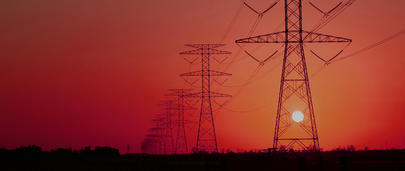 Silhouetted electricity pylons stand against a striking red sunset