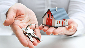 A person holds a house key in one hand and a model house in the other